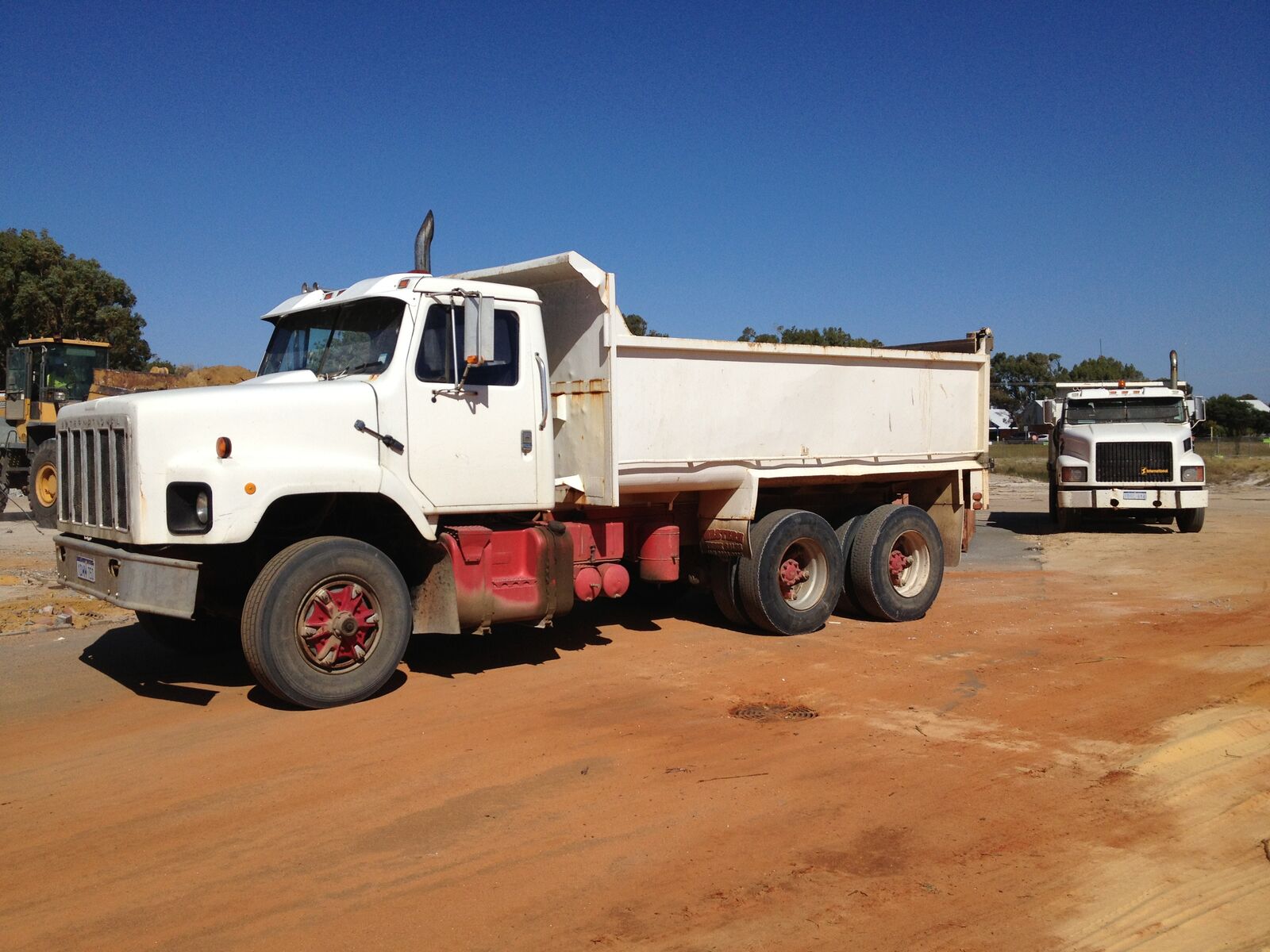 K & J International tipper on a cleared red dirt site with a second truck behind