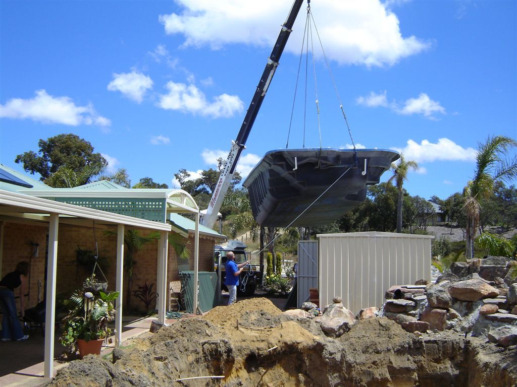 Crane lifting a fibreglass swimming pool off a truck into a backyard