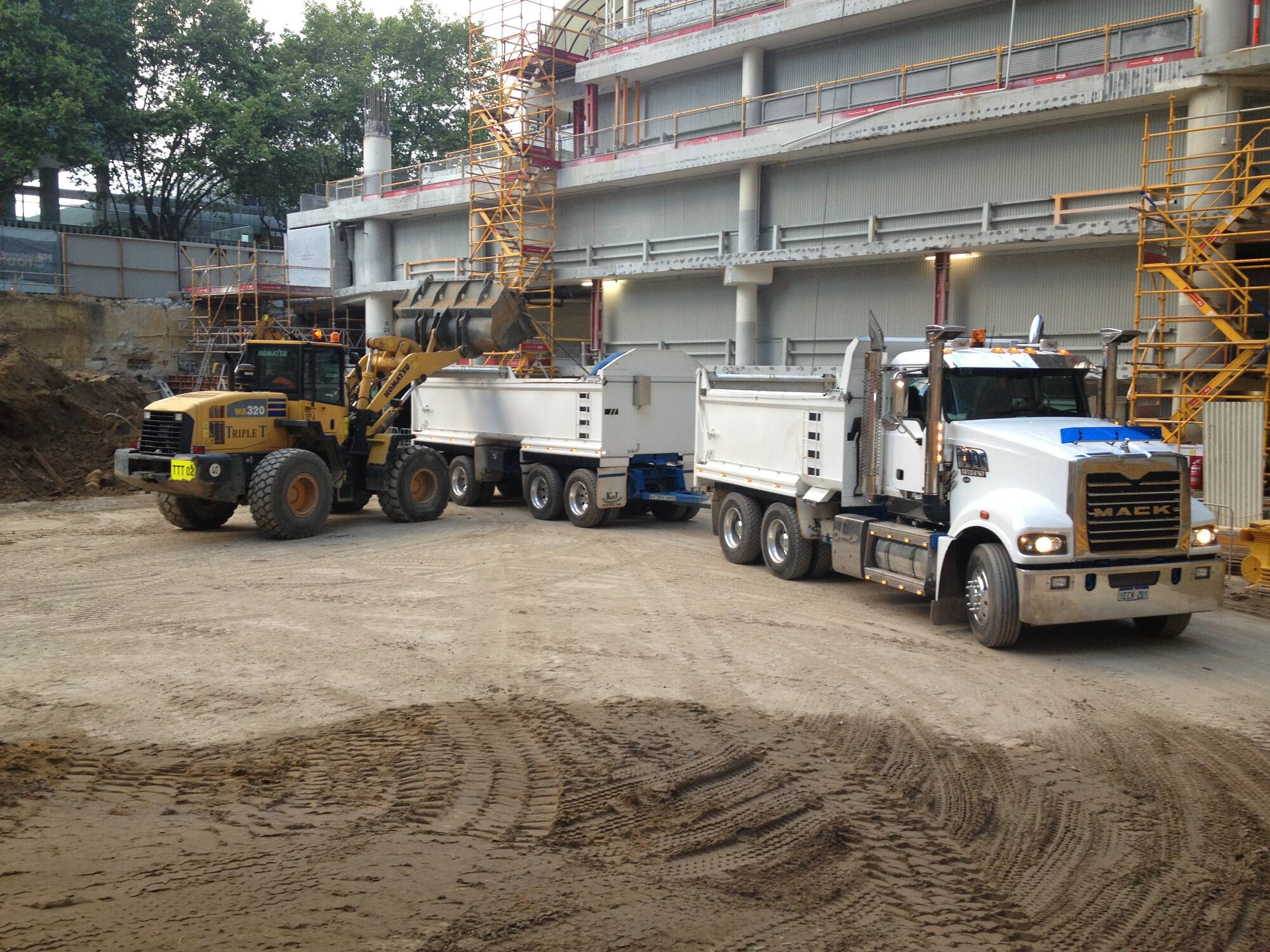 K & J Transport truck and dogs lined up with a loader on a city construction site at dawn