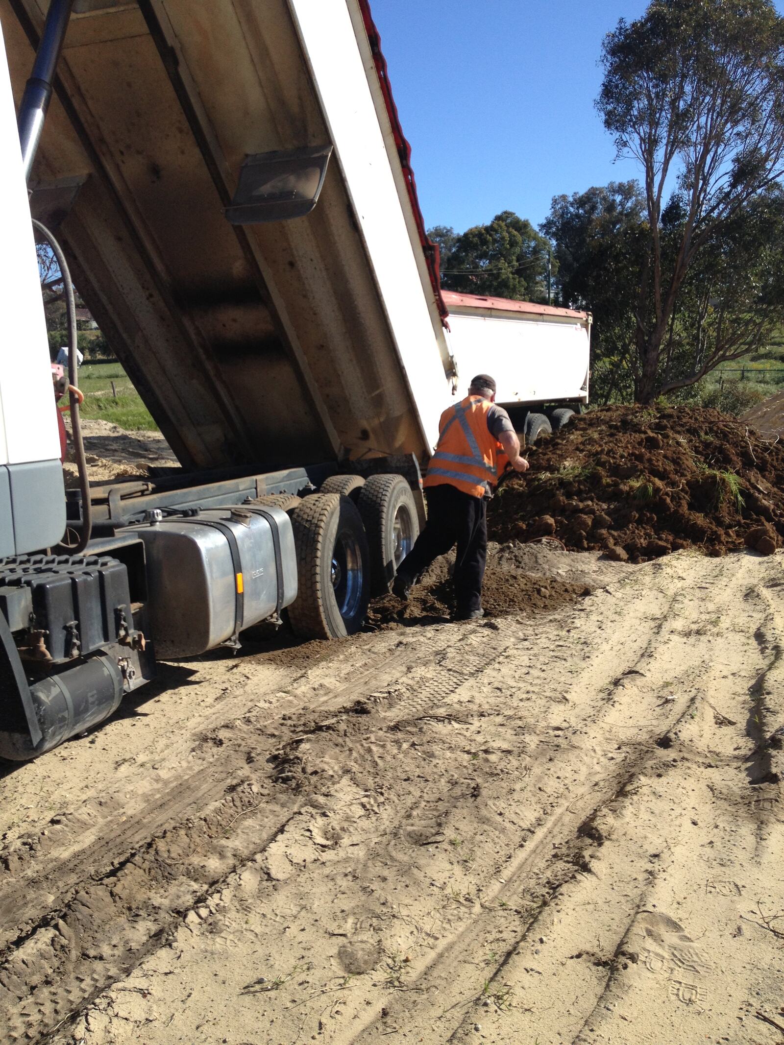 Tipper unloading soil on a bush block while the driver rakes it out